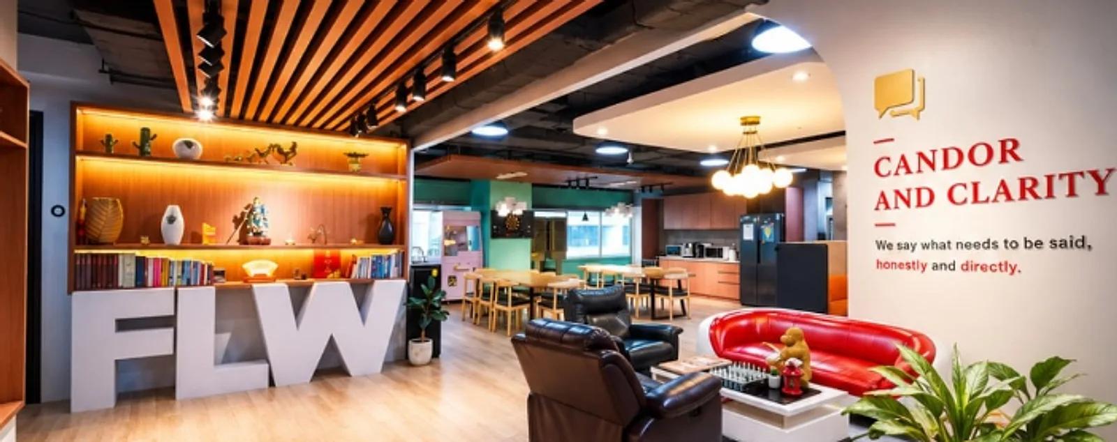 Office reception lounge with leather armchairs, a red sofa, lit wooden display shelves and a pantry area behind